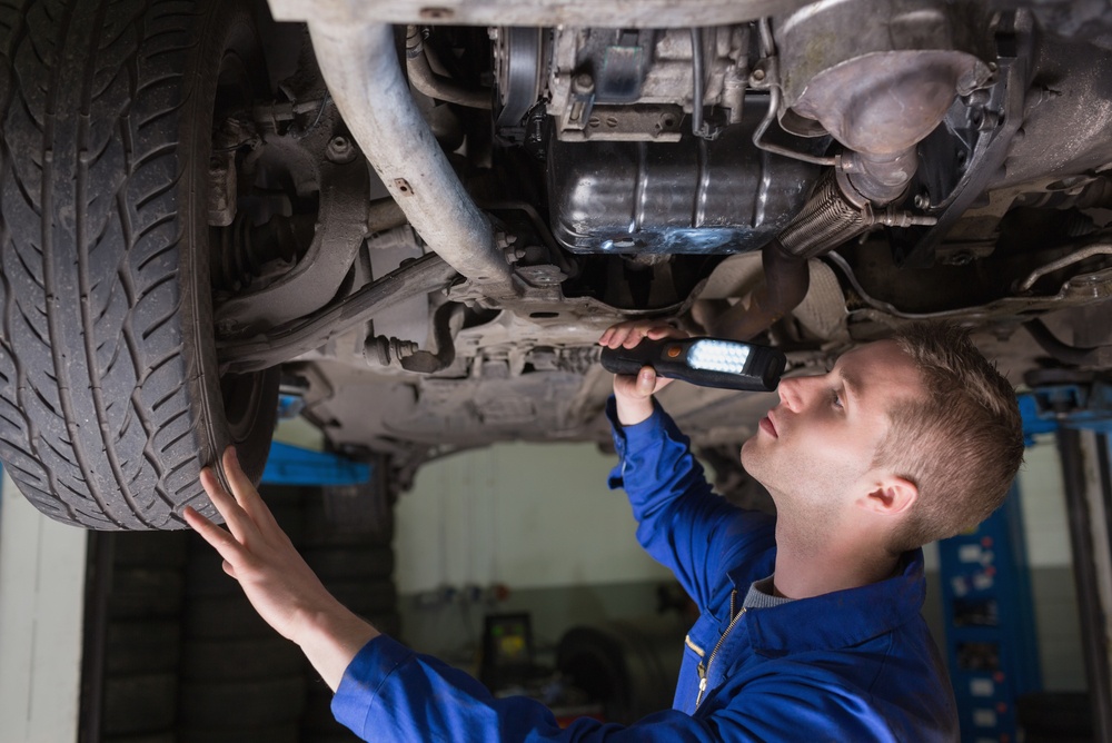 Male mechanic examining car using flashlight